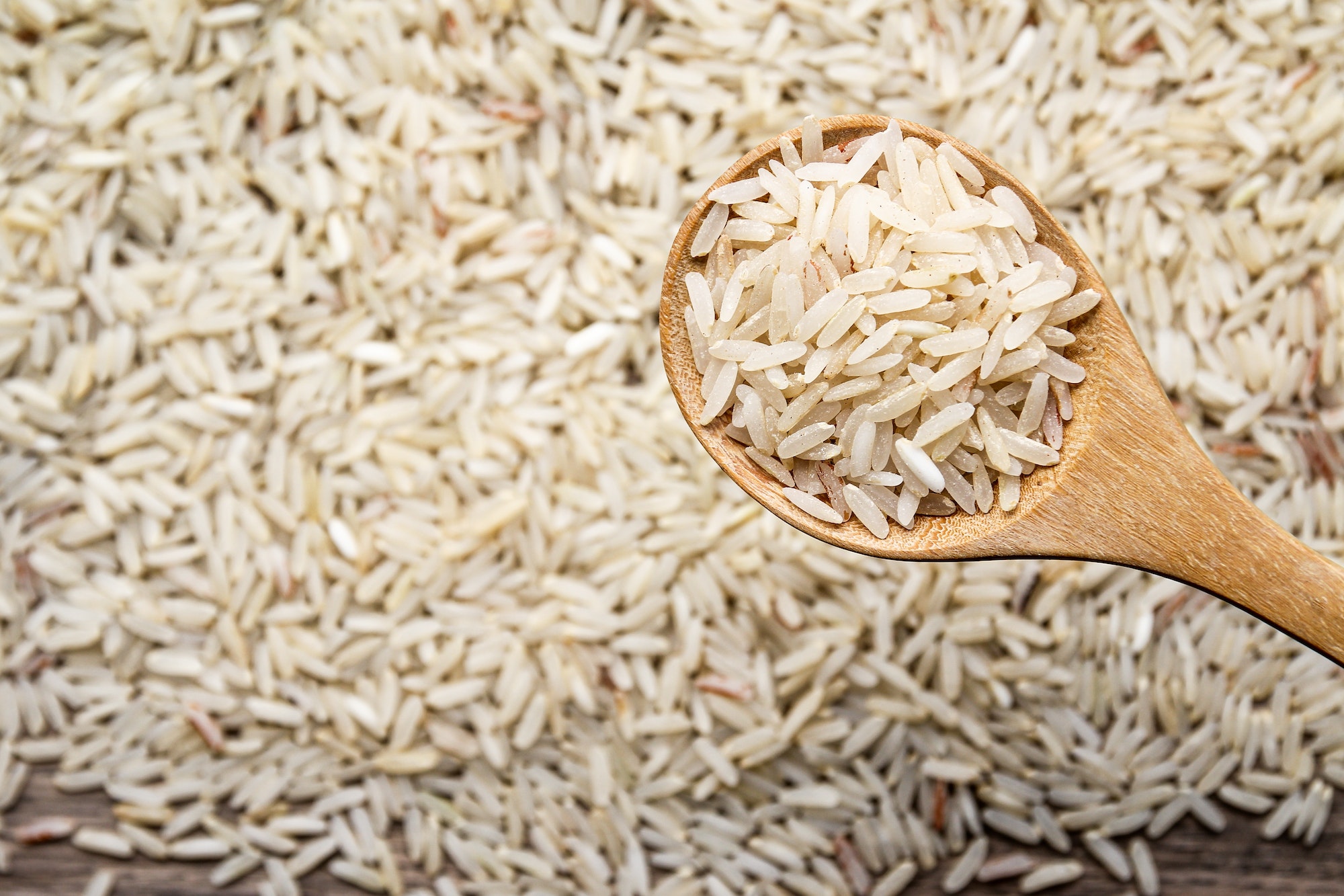 Clube da Horta - Arroz cru não orgânico em colher de pau em fundo de mesa de madeira velha